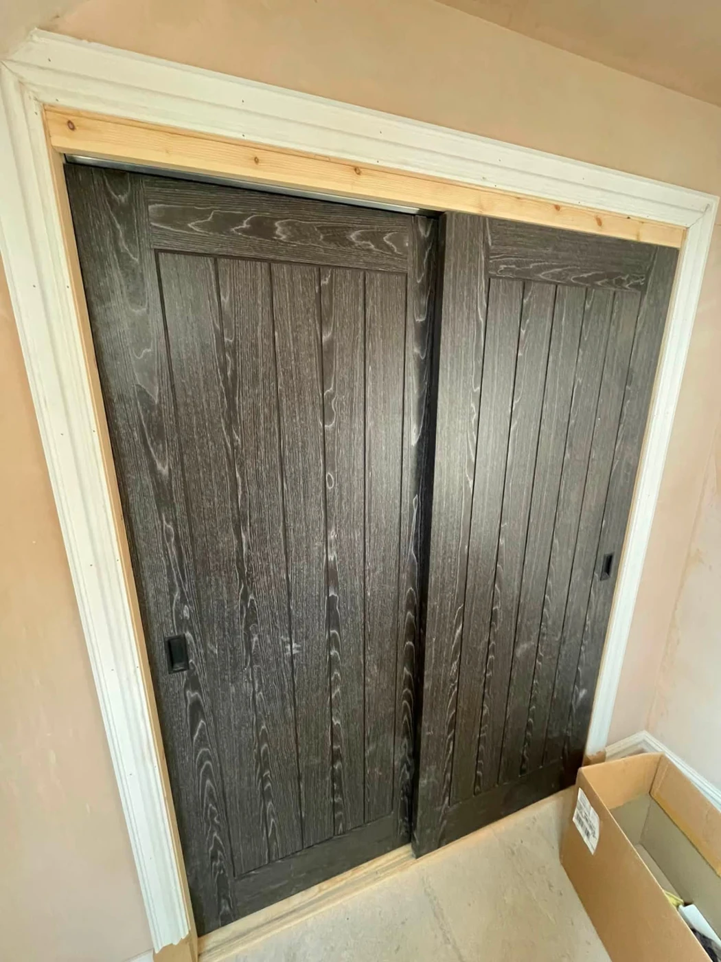 Dark timber sliding storage doors with recessed handles, before final finishing